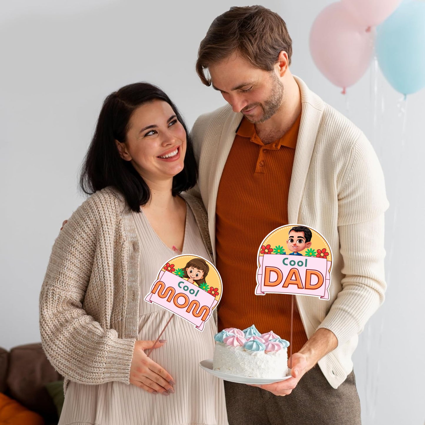 Pregnant woman and man holding a cake with 'Cool Mom' and 'Cool Dad' signs, balloons in the background.