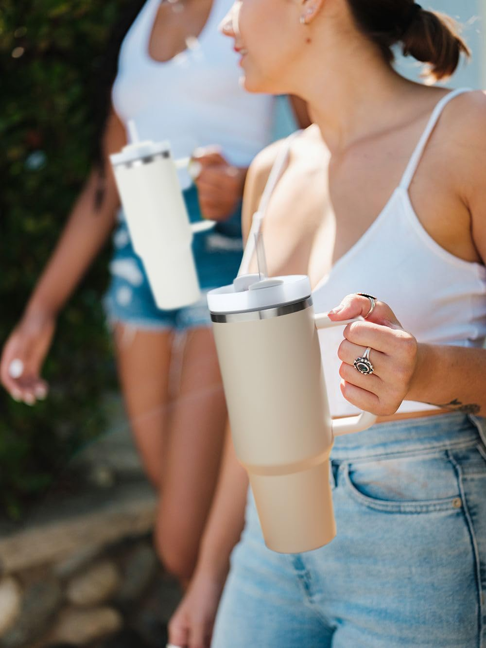 Woman holding a beige insulated tumbler outdoors with another person in the background.