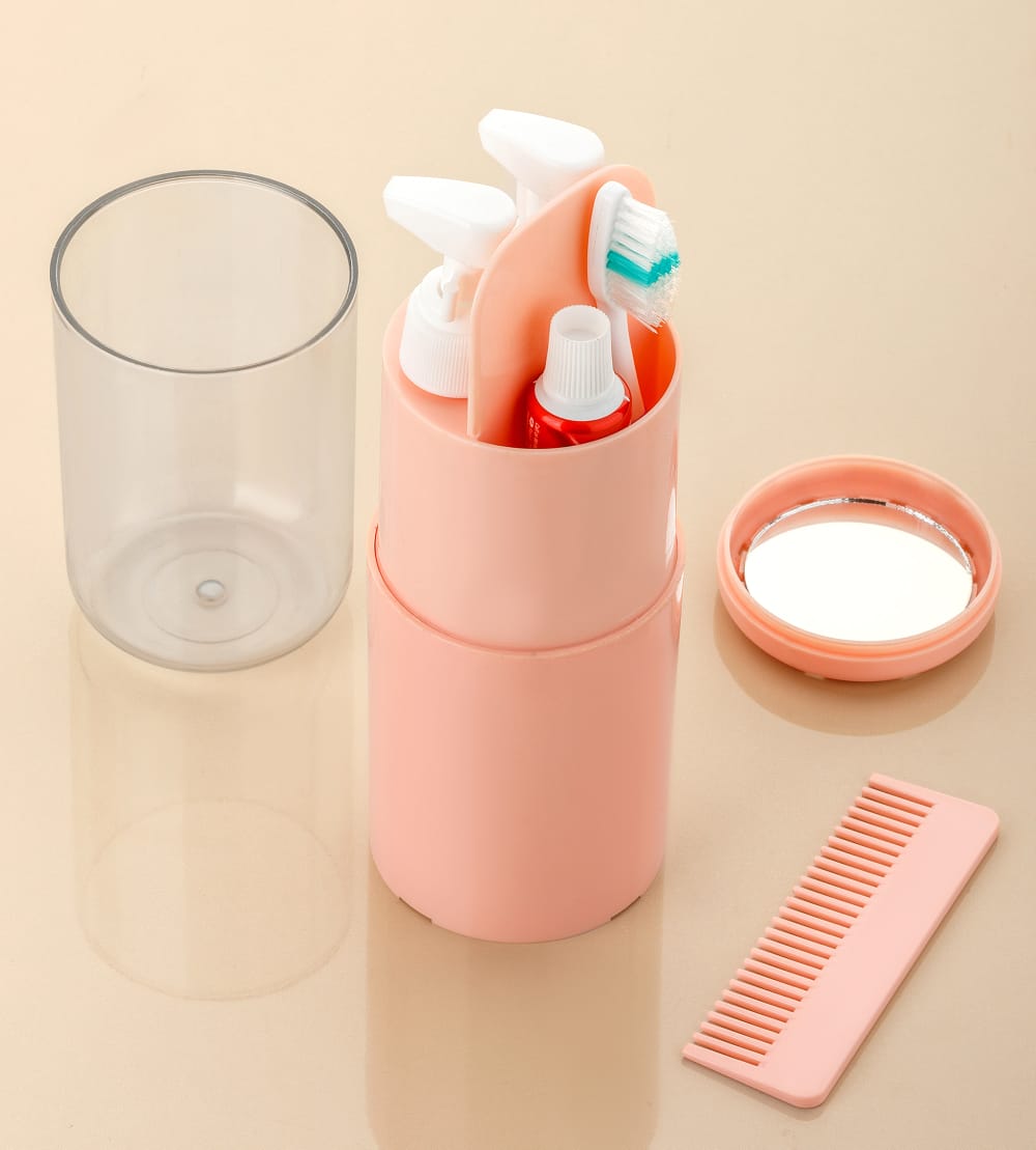 Pink travel toothbrush holder with toothbrushes, a glass, and a comb on a beige background