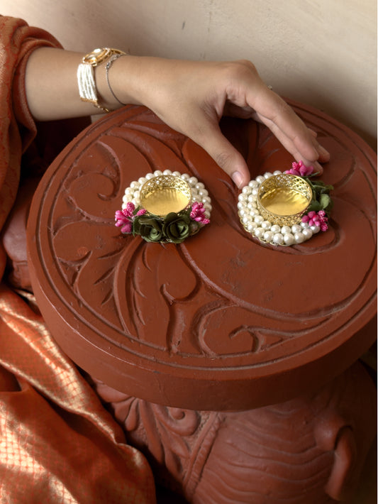 Decorative earrings with pearls and pink flowers on a brown round object.
