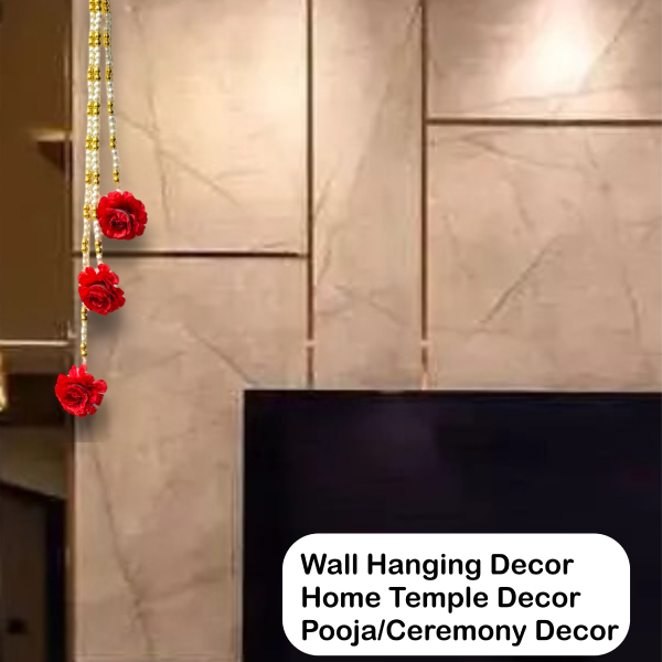 Decorative wall hanging with red flowers and gold strings on a tiled wall.