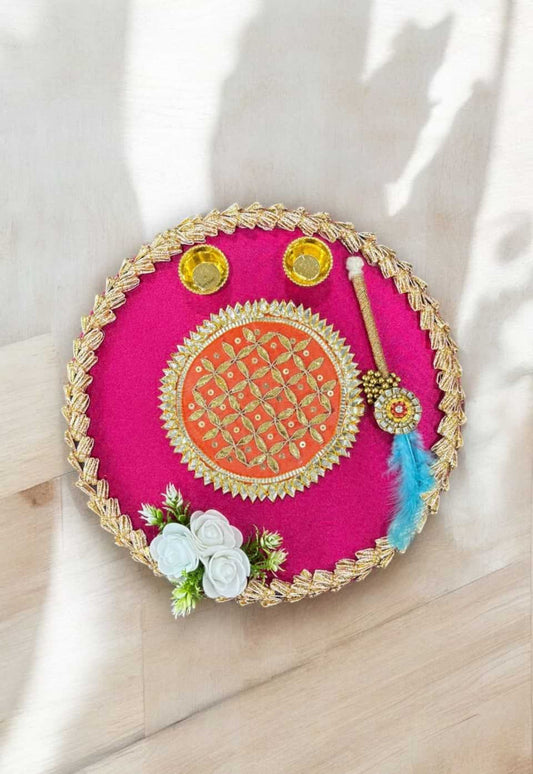 Decorative pink round tray with gold embroidery, flowers, and decorative items on a light background