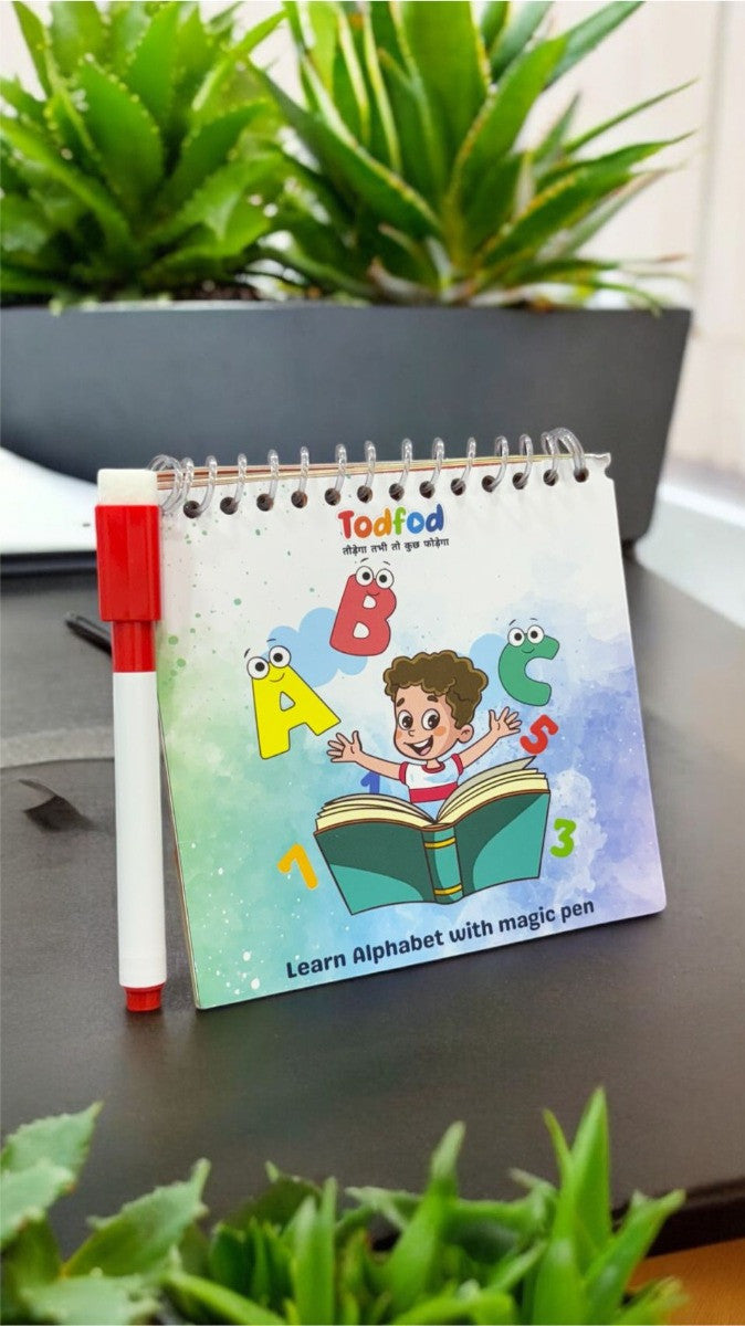 Children's book with alphabet illustrations and a magic pen on a desk with plants in the background