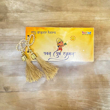Decorative item with tassels and beads on a yellow card with text, placed on a wooden surface.
