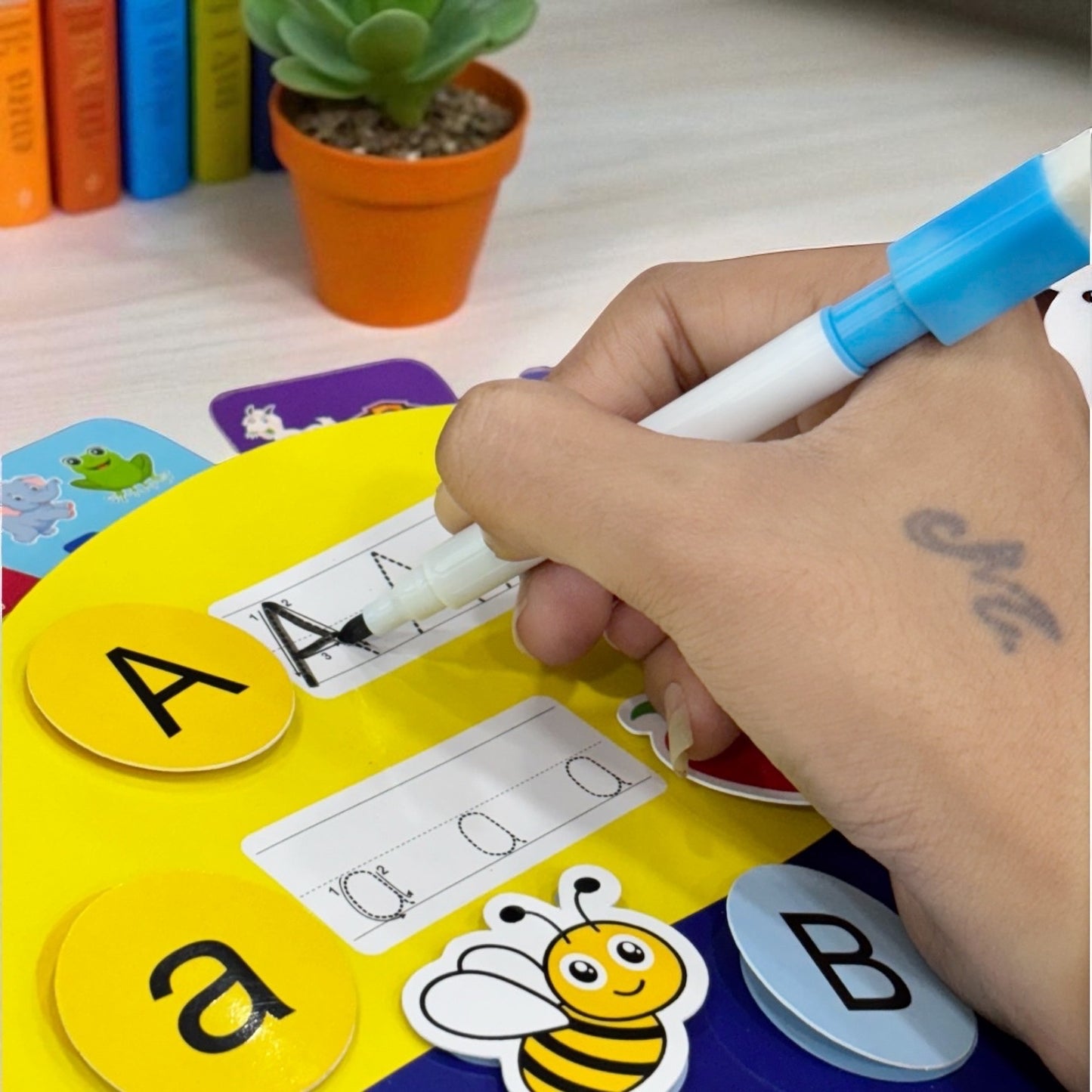 Hand writing on a letter recognition game with letters A and a, surrounded by educational materials.
