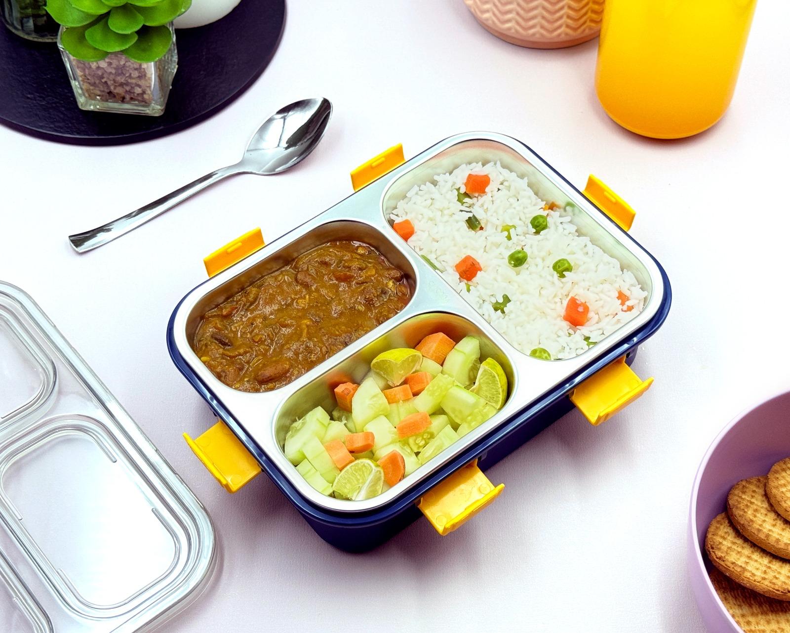 Meal container with compartments of food on a table with a spoon and drink.