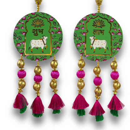 Pair of decorative earrings with green circular designs featuring cows, gold and pink tassels on a white background.