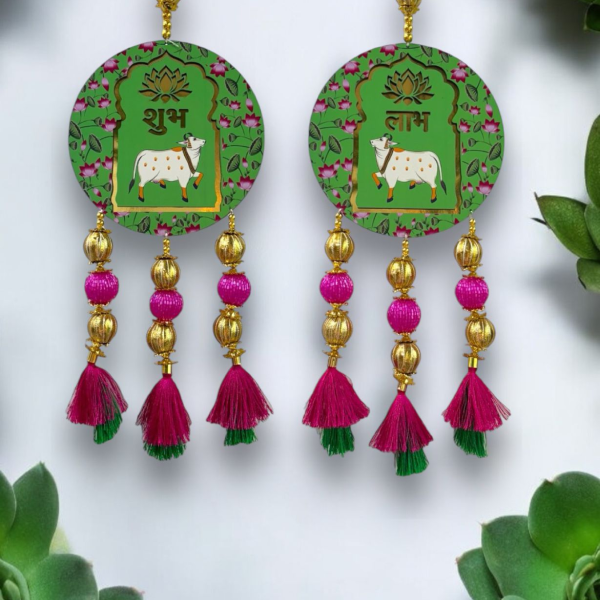 Pair of earrings with green circular designs featuring cows, gold and pink beads, and tassels on a white background.