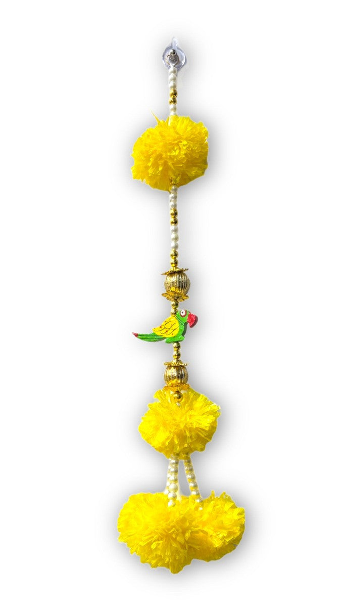 Decorative hanging with yellow pom-poms and a small bird figurine on a white background