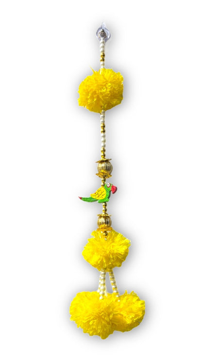 Decorative hanging with yellow pom-poms and a small bird figurine on a white background