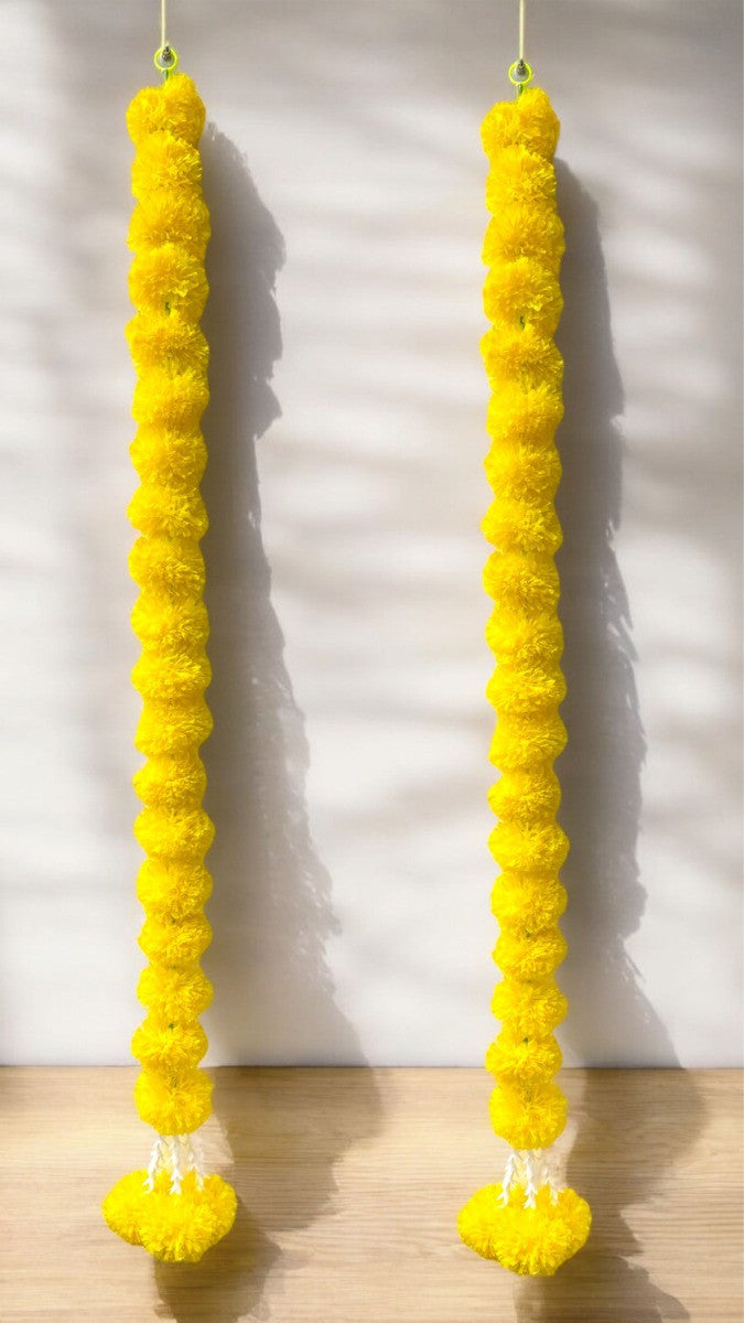 Two yellow decorative strings with pom-poms hanging against a white wall.